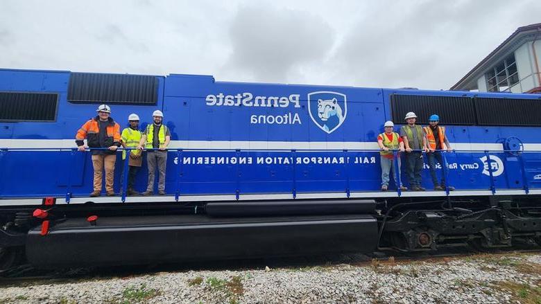 Rail Transportation Engineering students and faculty pose with a Penn State-branded locomotive